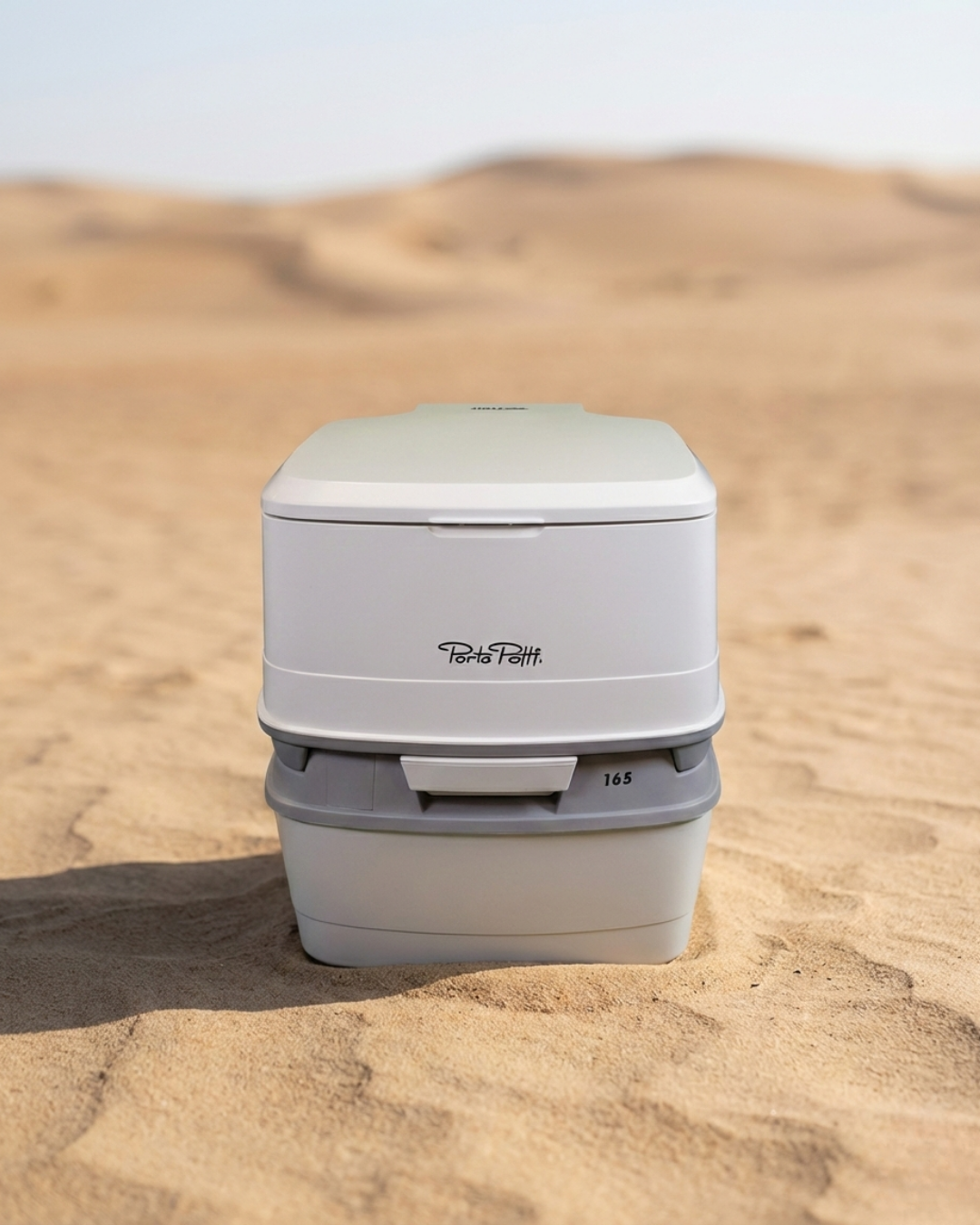 Portable toilet in the sand with 'Porta Potti' branding